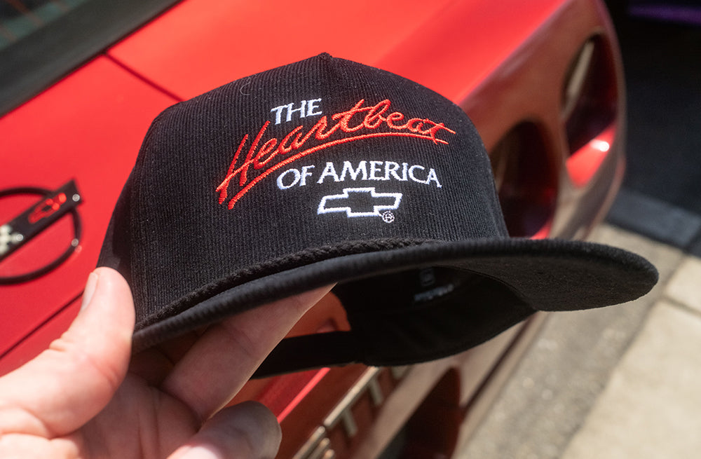 HWV x Chevrolet Heart Beat of America Black Corduroy Hat in front of a corvette.