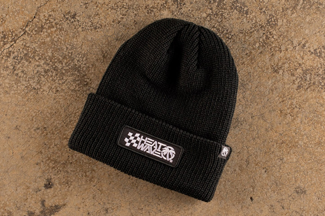 Lying on the concrete is the Heat Wave Visual Racing Black Beanie.