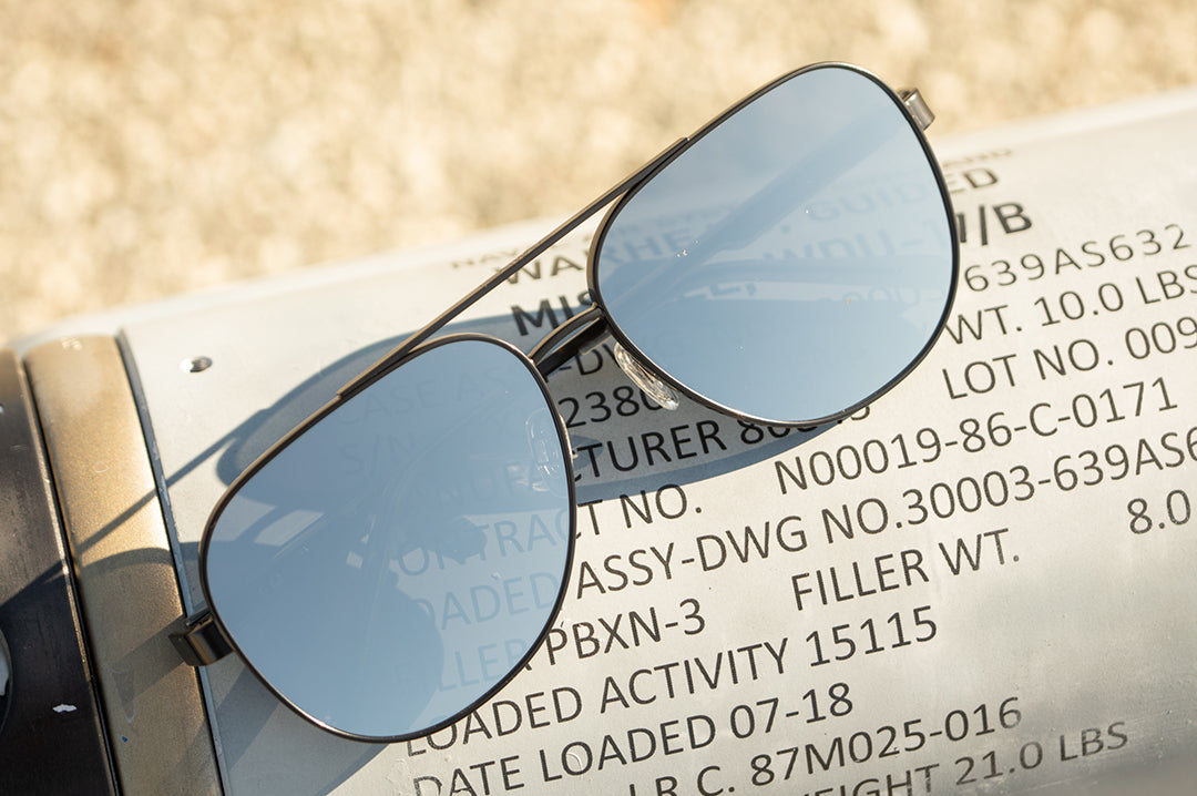 Lying on a metallic surface is the Heat Wave Visual Incline Sunglasses with gun metal frame and silver lenses.
