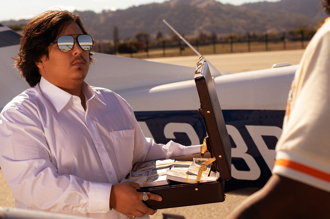 Zack holding a brief case full of cash while wearing the Heat Wave Visual Incline Sunglasses with gun metal frame and silver lenses.
