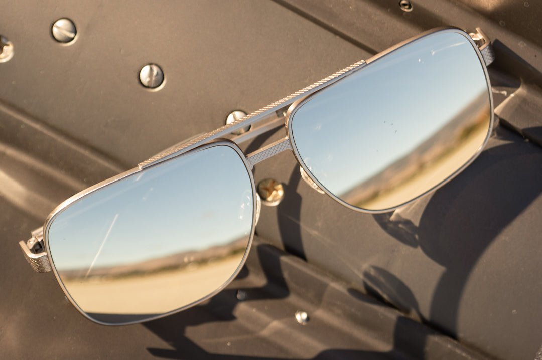 Heat Wave Visual Nimitz Sunglasses with gun metal frame and silver lenses sitting on a metallic surface.