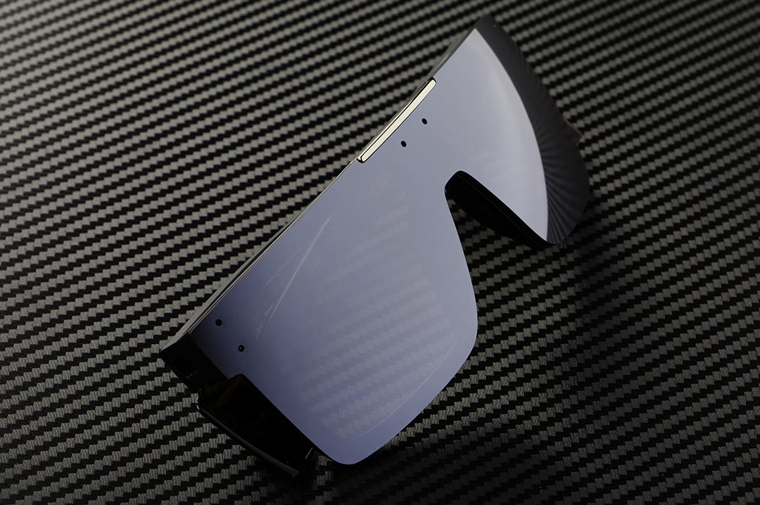 Sitting on a a table is the Heat Wave Visual Performance Quatro Sunglasses with black frame, silver lens and matching colored side shields.