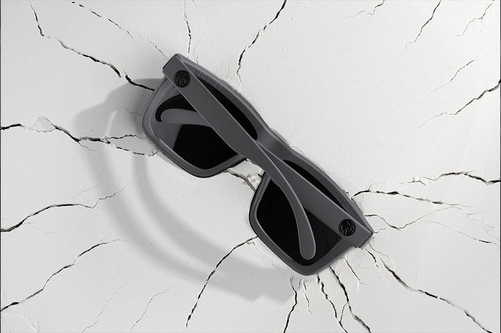 Back of Heat Wave Visual Vise Sunglasses with satin grey frame and black lenses on cracked white surface.