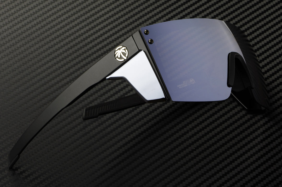 Laying on a table is the Heat Wave Visual Performance Lazer Face Sunglasses with black frame, silver lens and matching colored side shields.