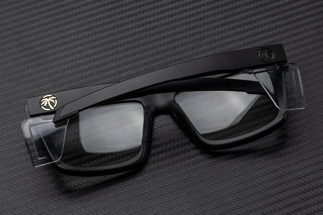 Laying on a table is the Heat Wave Visual Performance XL Vise Sunglasses with black frame, anti-fog clear lenses and clear side shields.