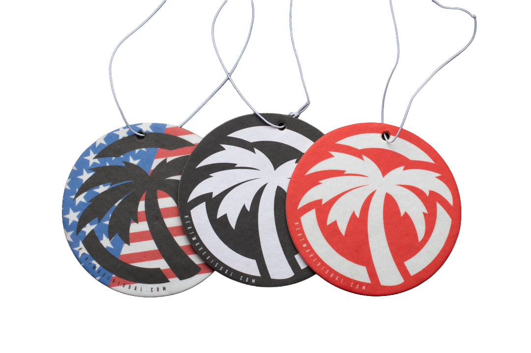 Three round hanging air freshener or car fragrance discs with white string loops, shown on a plain white background. The left disc has a blue, white, and red American flag and palm tree design.