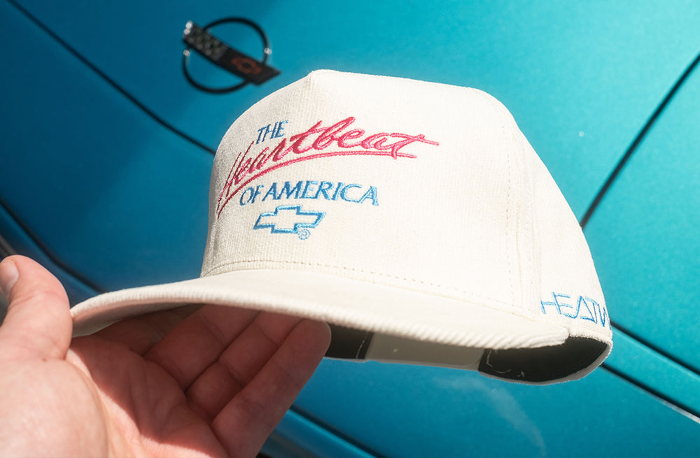 HWV X Chevrolet Heart Beat of America Off-white Hat in from of a C4 Corvette.