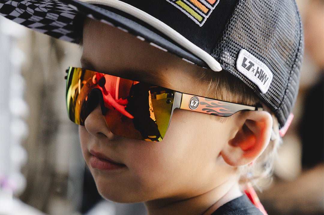 Young boy wearing the Kids Lazer Face Sunglasses: Little Trouble X Heat Wave Flames with red-orange gradient lens.