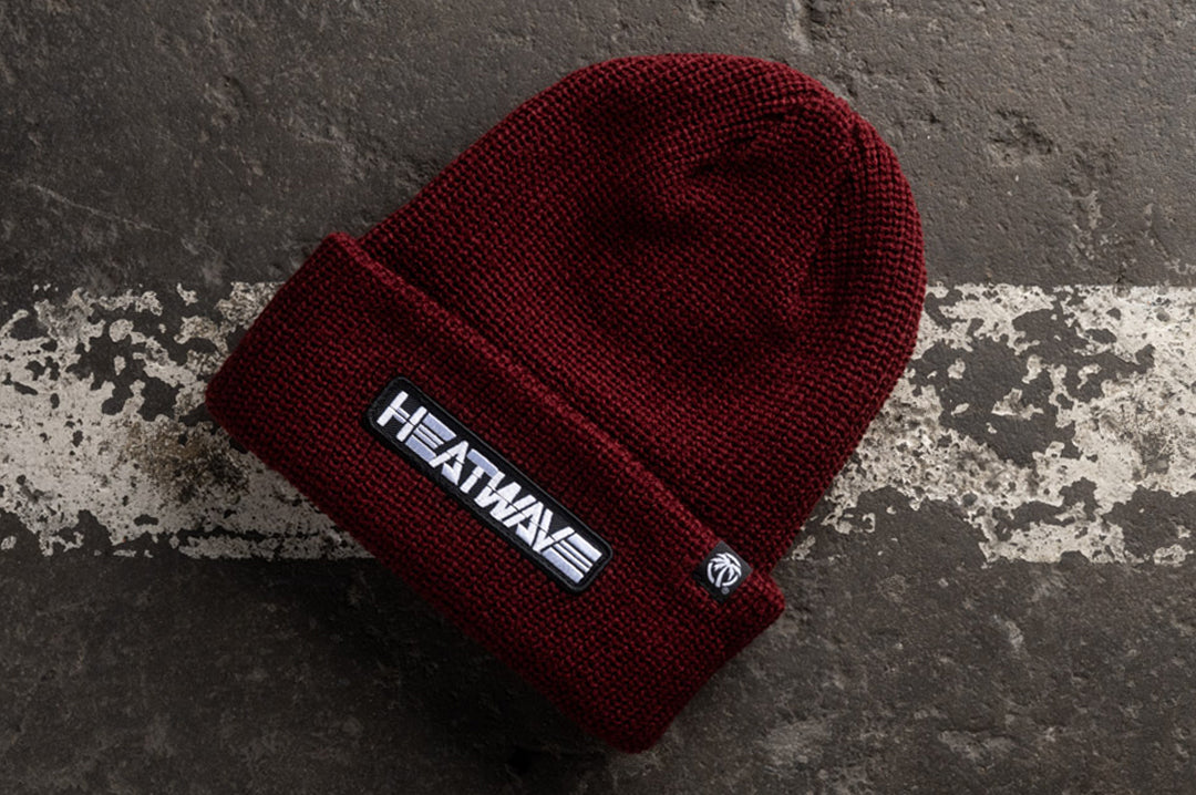Lying on the concrete is the Heat Wave Visual Cardinal Red Billboard Beanie.
