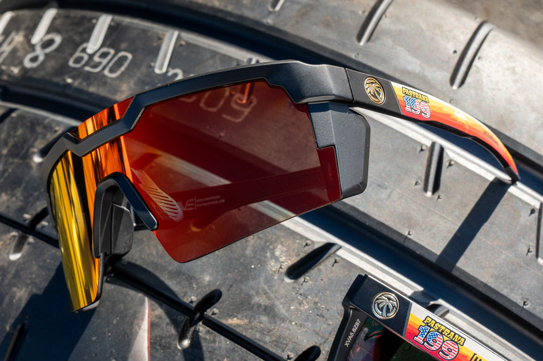 Lying on a tire is the Heat Wave Visual Future Tech Sunglasses with black frame, Hoonigan Pastrana print arms and sunblast lens.