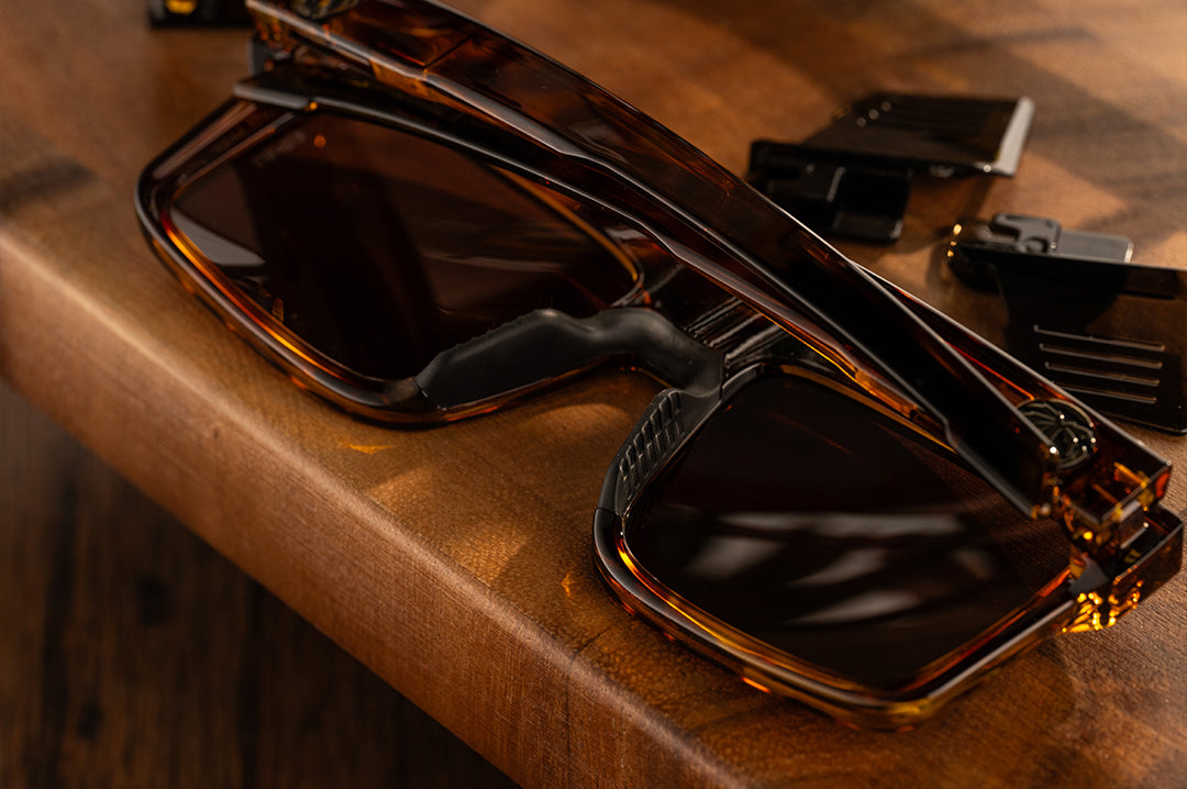 Close up shot of the Performance Rayth Sunglasses: Tortoise Z87+ with brown side shields lying on a wood table. 
