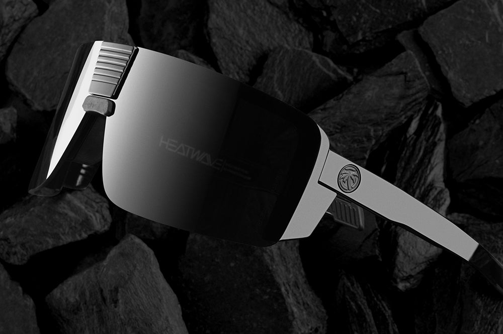 Lying on top of black rocks is the Heat Wave Visual Vector Sunglasses with gloss black frame and ultra black lens.