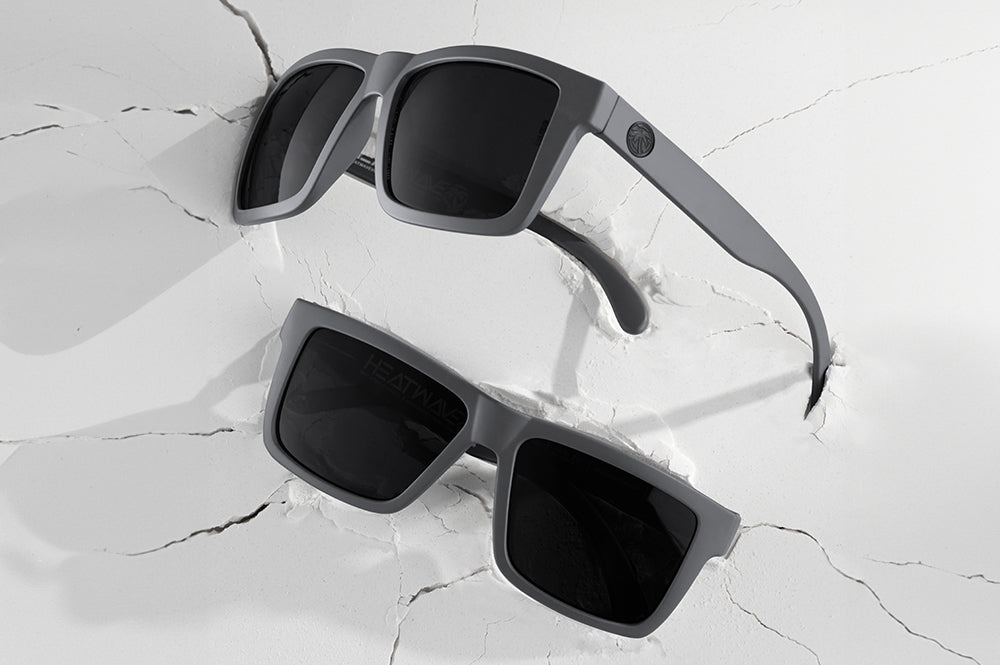 2 pairs of Heat Wave Visual Vise Sunglasses with satin grey frame and black lenses on cracked white surface.