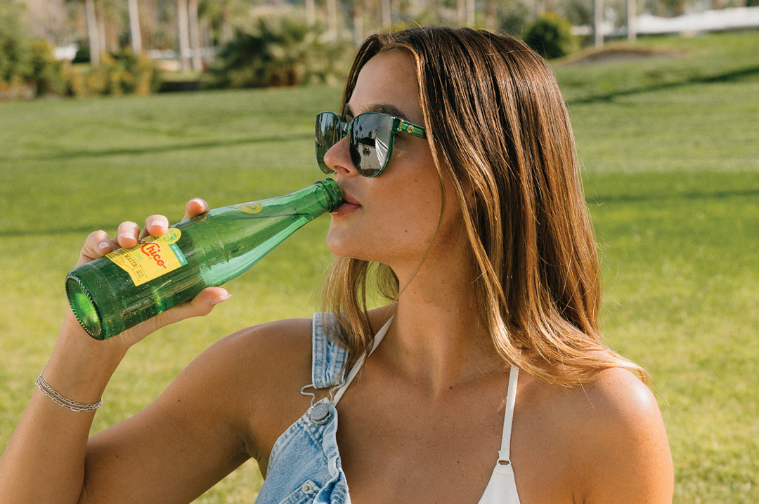 Woman wearing the Carat Sunglasses: Cycad Green drinking topo chico