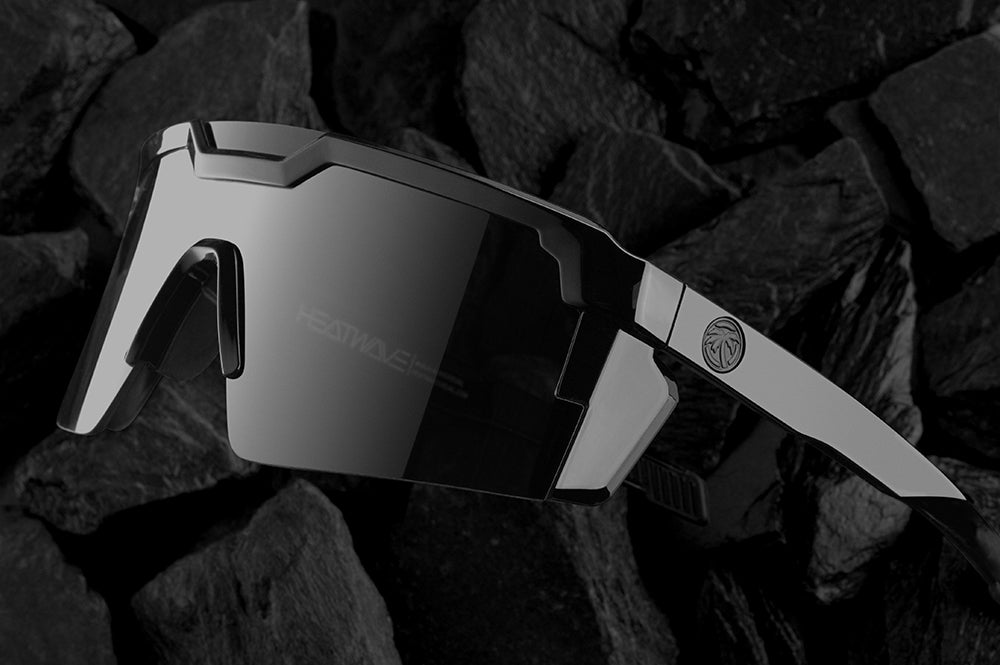 Lying on top of black rocks is the Heat Wave Visual Future Tech Gloss Black Sunglasses.