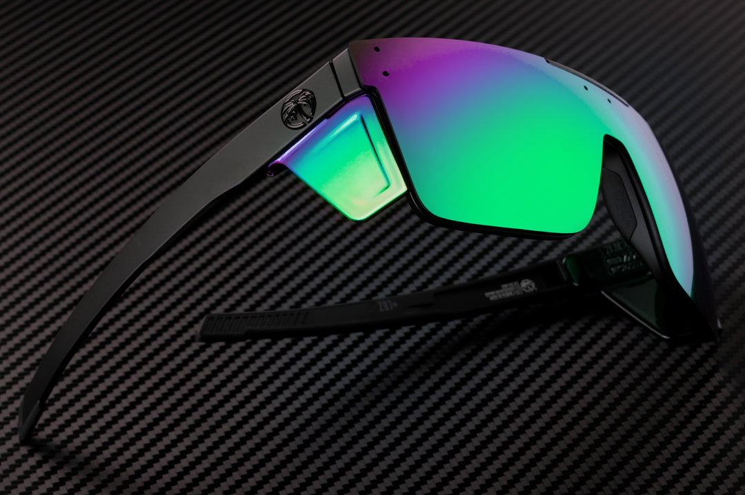 Laying on a table is the Heat Wave Visual Performance Quatro Sunglasses with black frame, piff green blue lens and matching colored side shields.