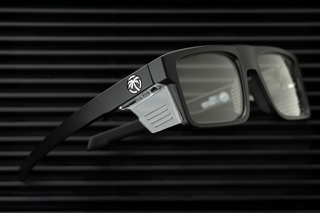 Lying on a table is the Heat Wave Visual Performance Rayth Sunglasses with black frame, anti-fog clear lenses and clear side shields. 