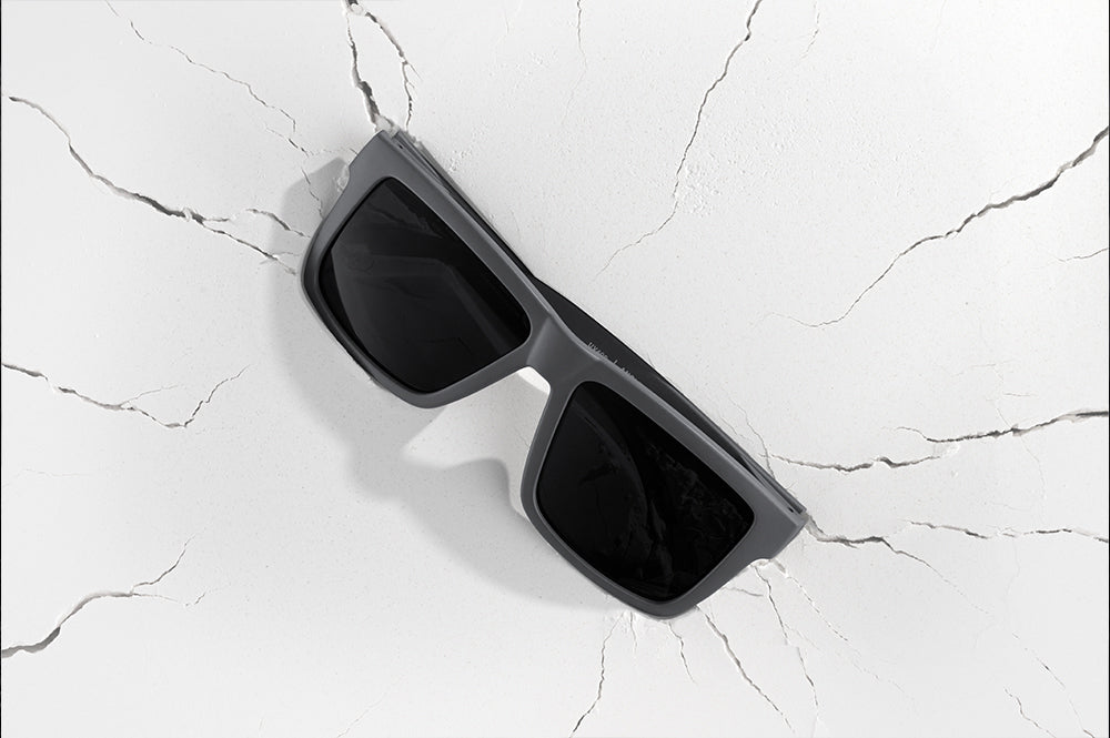 Heat Wave Visual Vise Sunglasses with satin grey frame and black lenses on cracked white surface.