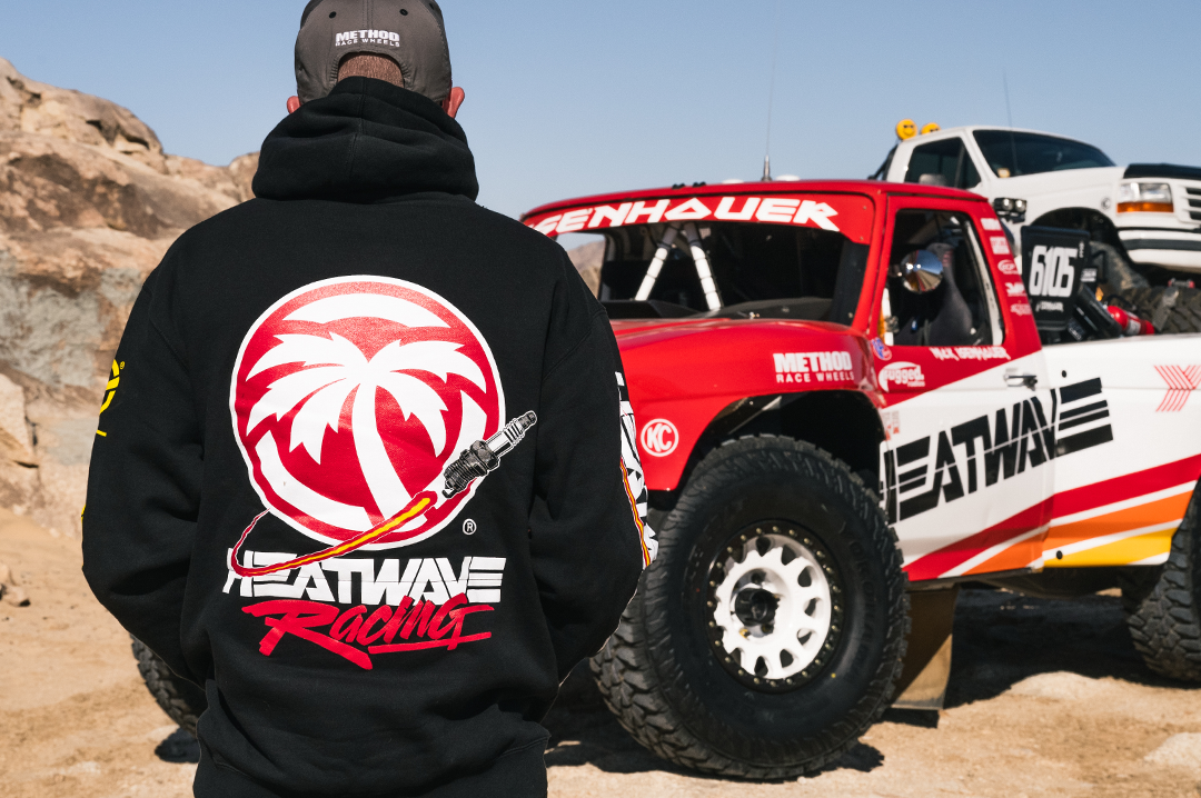 Eisenhouer brother wearing a black hoodie with a palm tree logo and 'Heatwave Racing' text, standing in front of a red and white off-road vehicle.